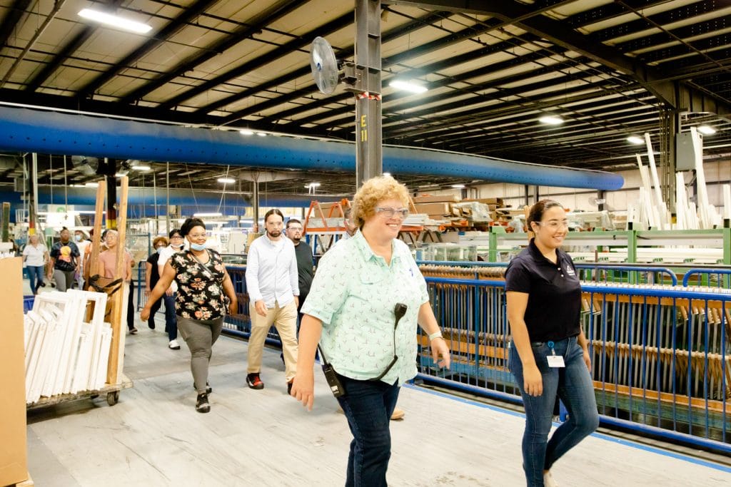 Group of people wearing safety glasses being led through glass production warehouse